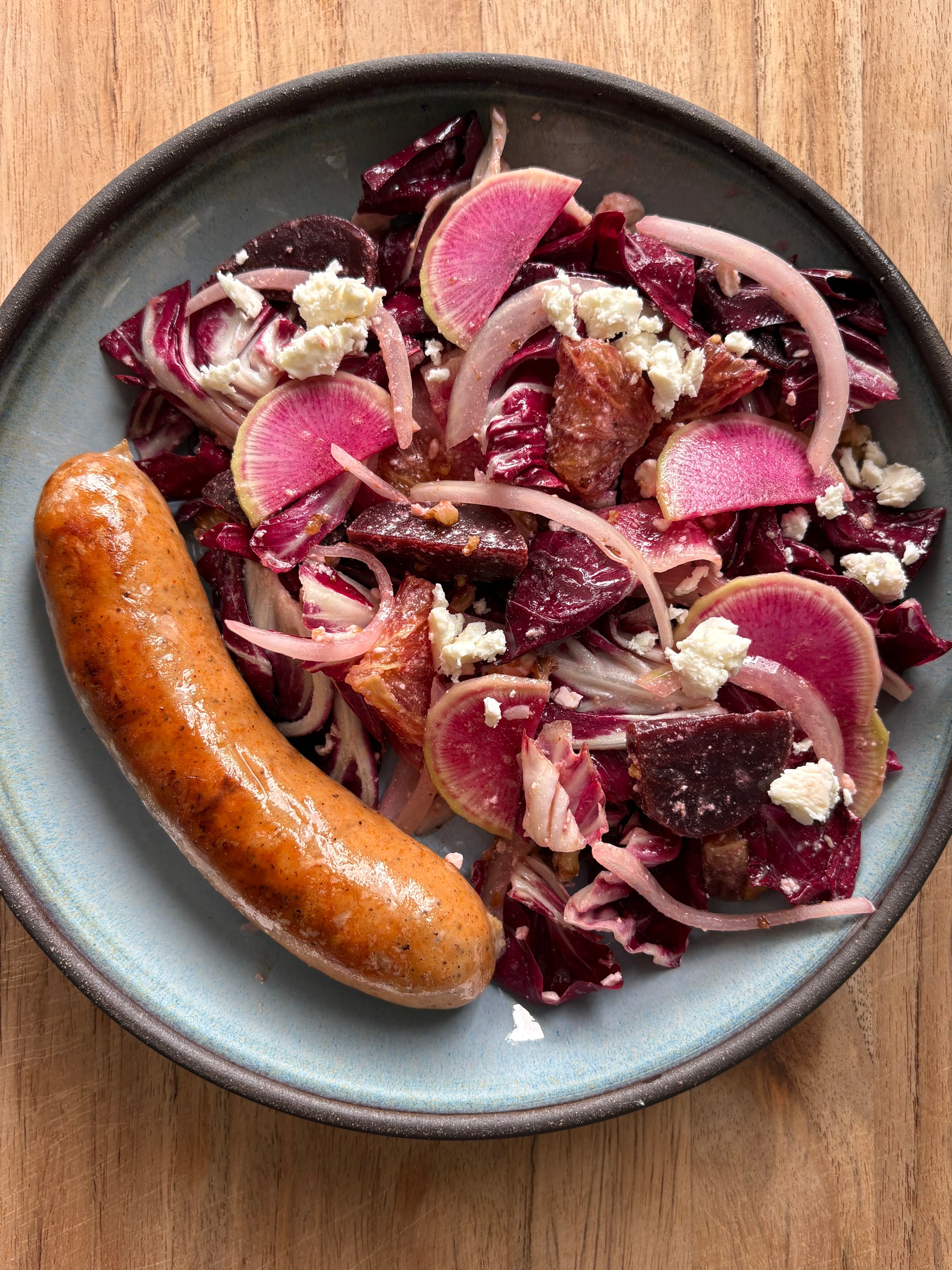 Plate of pink salad with radishes and a sausage on a wooden table