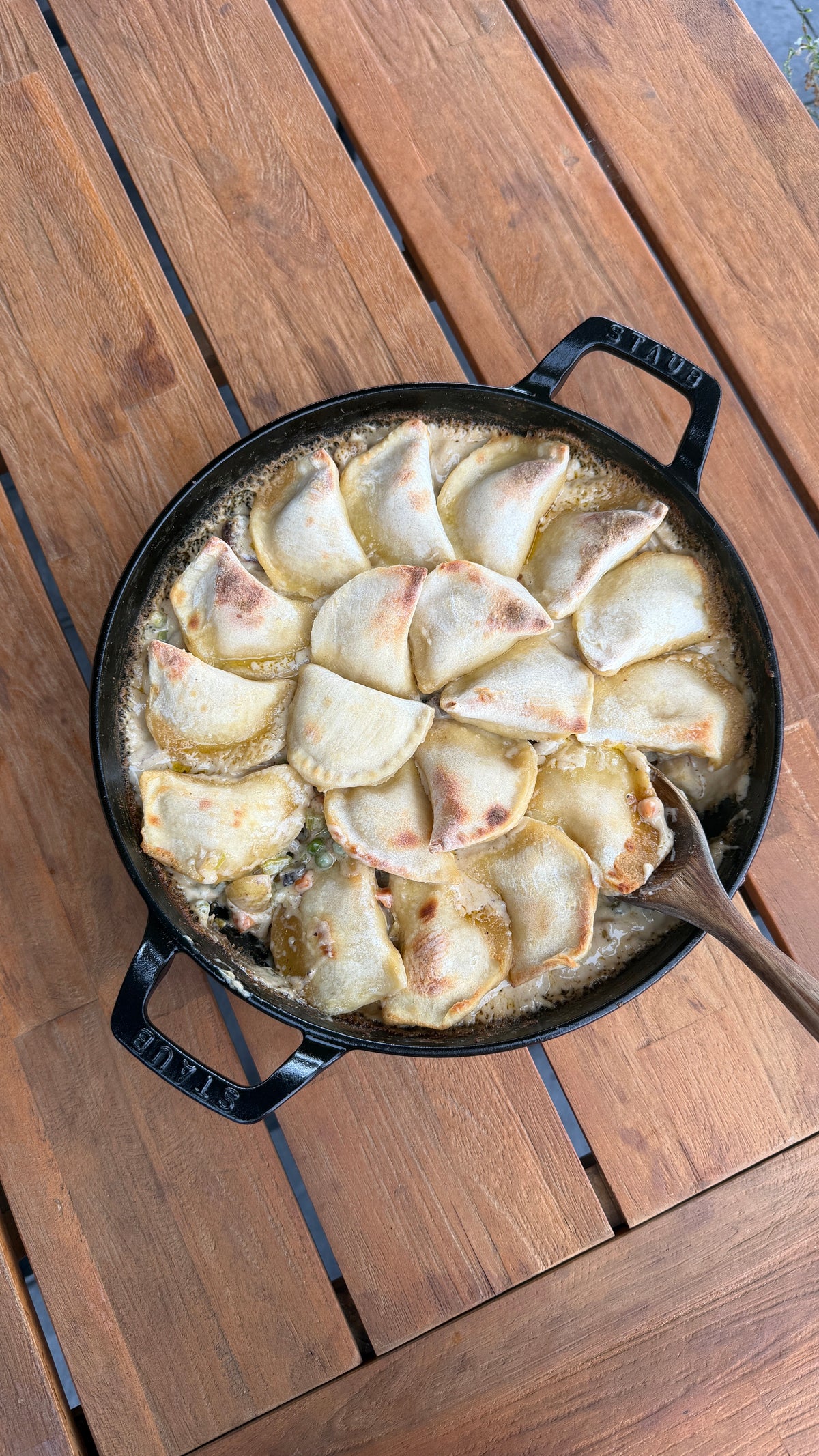 pierogi covered pot pie in a skillet on a wooden table with a wooden spoon