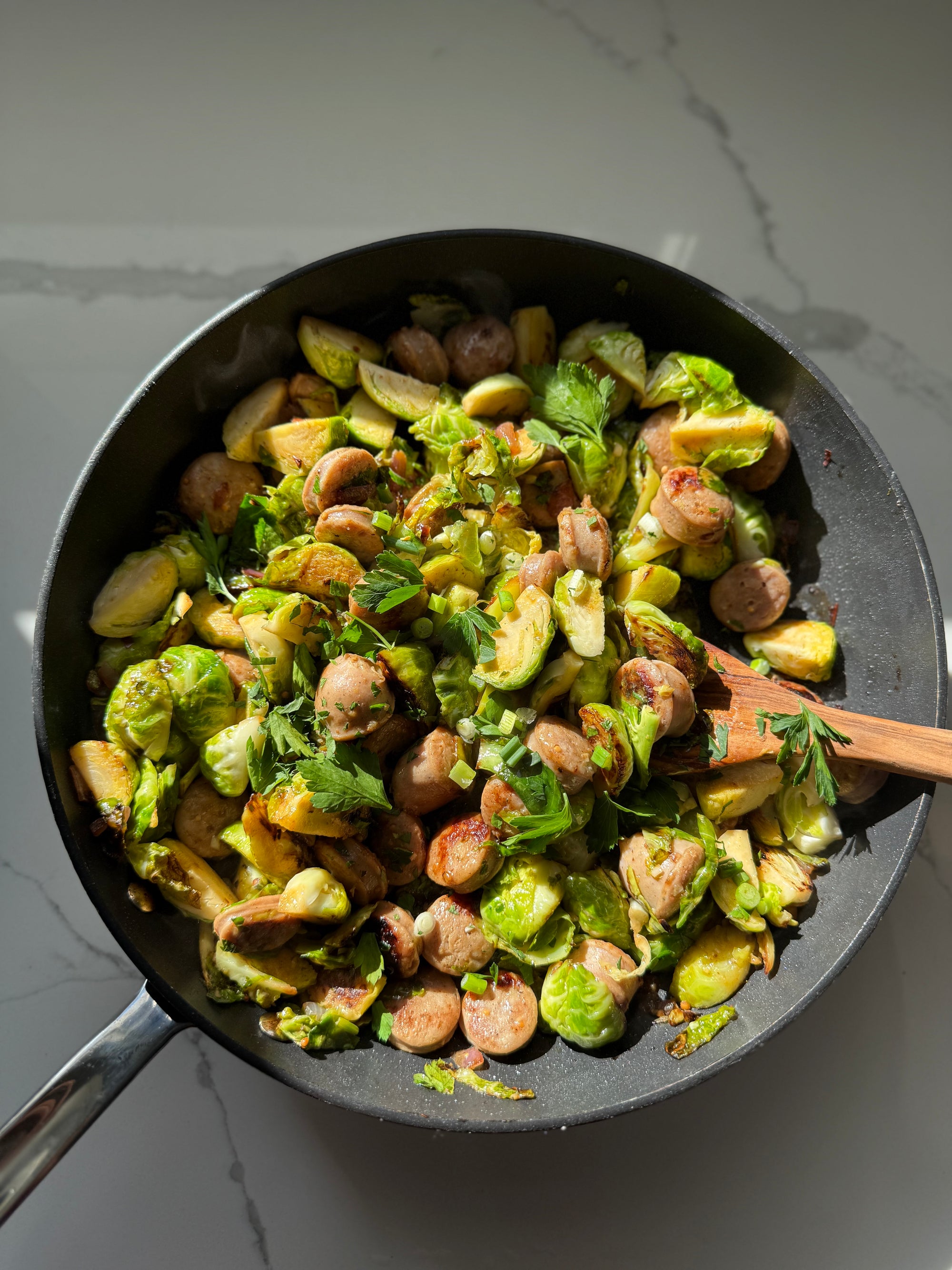 Fried brussels sprouts with sausage in a frying pan on a marble countertop