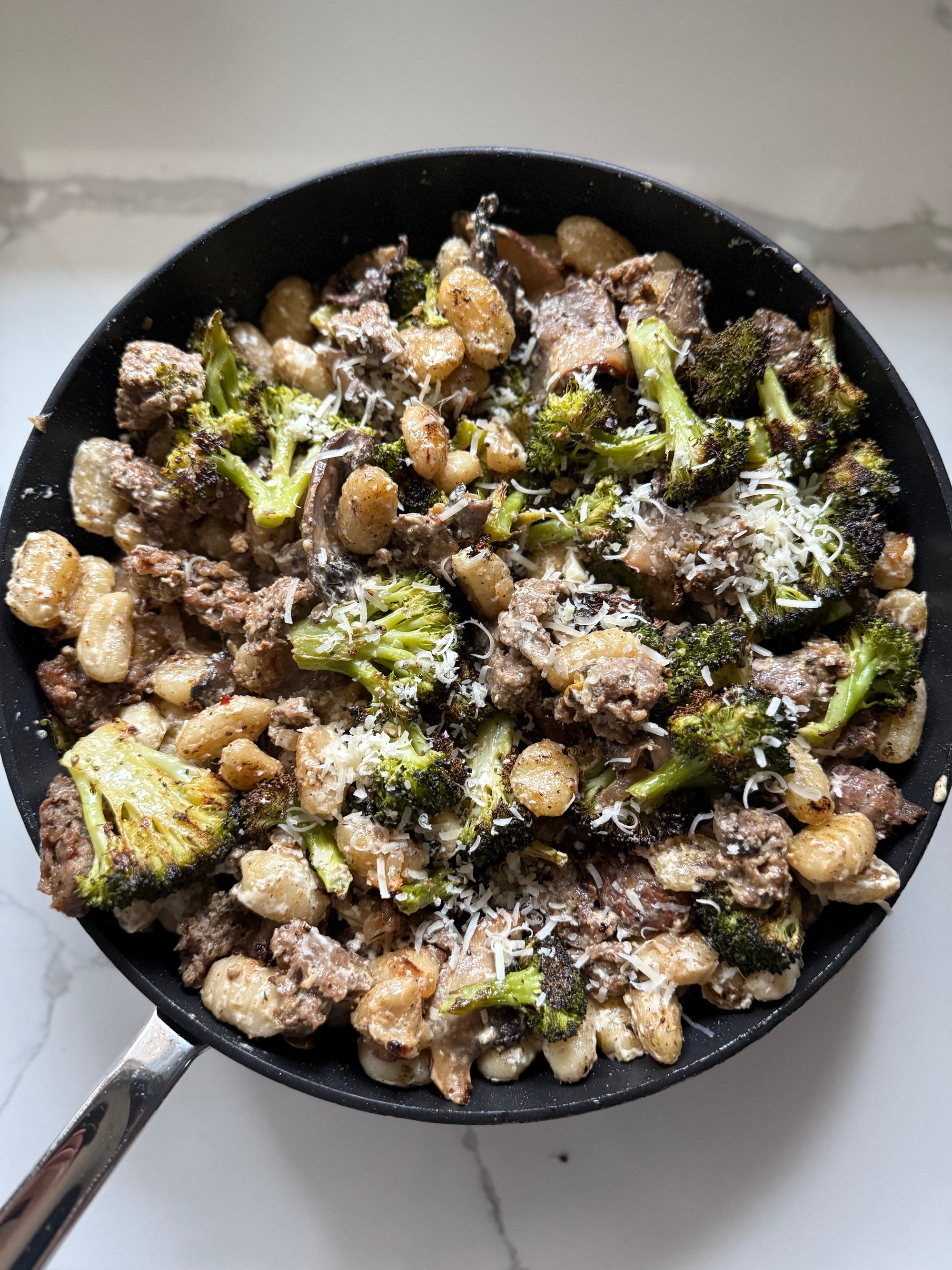 Fried gnochhi pasta with broccoli and ground meat in a black pan on a white surface