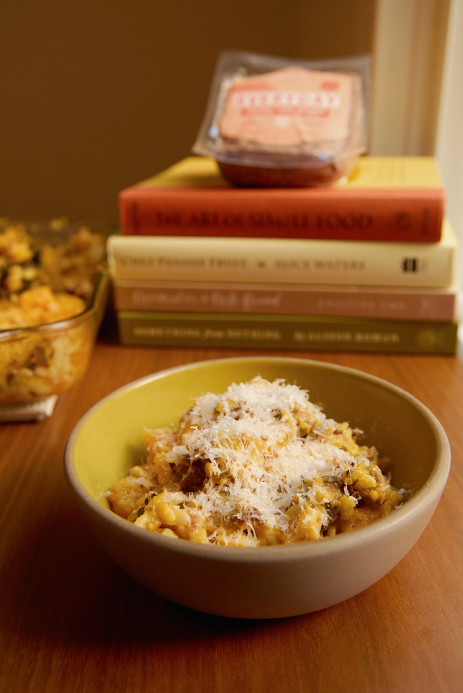 bowl of orzo sausage pasta on a table with books, sausage pack and baking dish in the background 