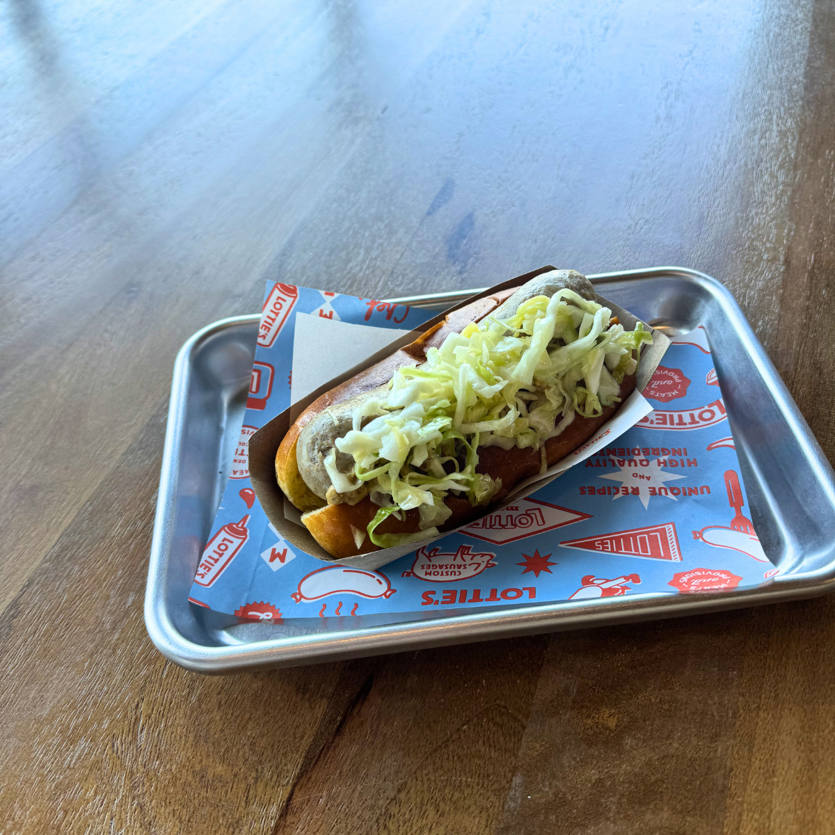 Lottie's sausage link with coleslaw on a tray with a branded paper underneath, on a wooden surface.